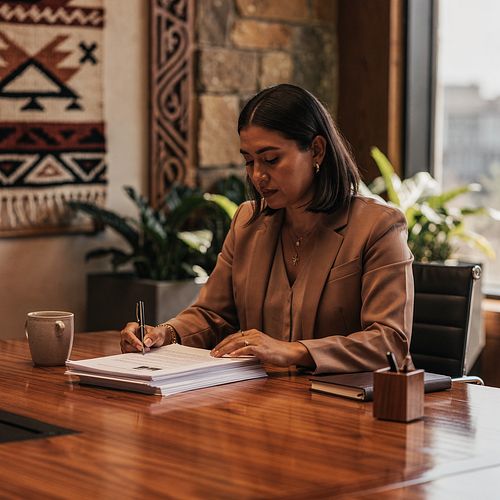 An Indigenous governance professional reviewing a bound set of Board minutes at a polished wood table.